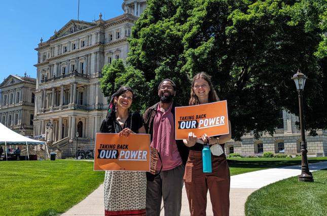 Michigan staff holding Taking Back Out Power signs in front of the State Capitol 