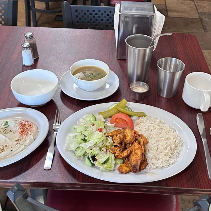 Shawarma meal set out on ceramic plates and bowls with stainless steel utensils and sauce cups