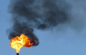 Gas flare fire and black smoke on blue sky day. 