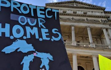 Sign outside Michigan state capitol building: "Protect our H.O.M.E.S." and image of the Great Lakes. Credit Jen Schlicht