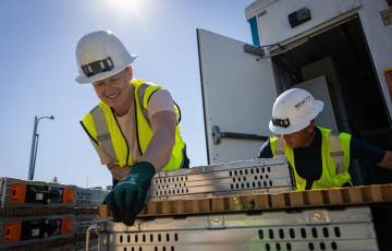 Two workers in safety gear unloading crates of battery packs