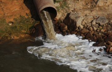 Corroded pipe sprewing direty water into a stream