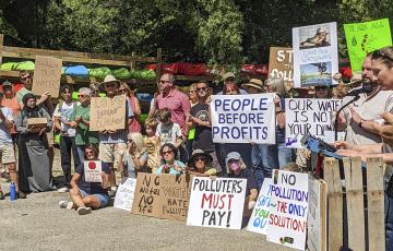 Polluter Pay rally with many attendees holding signs 