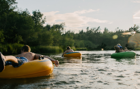 A family tubing on a river with text: What’s in Our Water Is in Our Brains: A Minnesota Perspective for Brain Awareness Week
